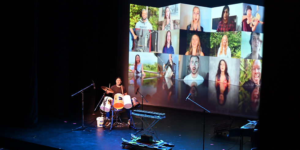 a man playing drums in front of a screen with people on it.