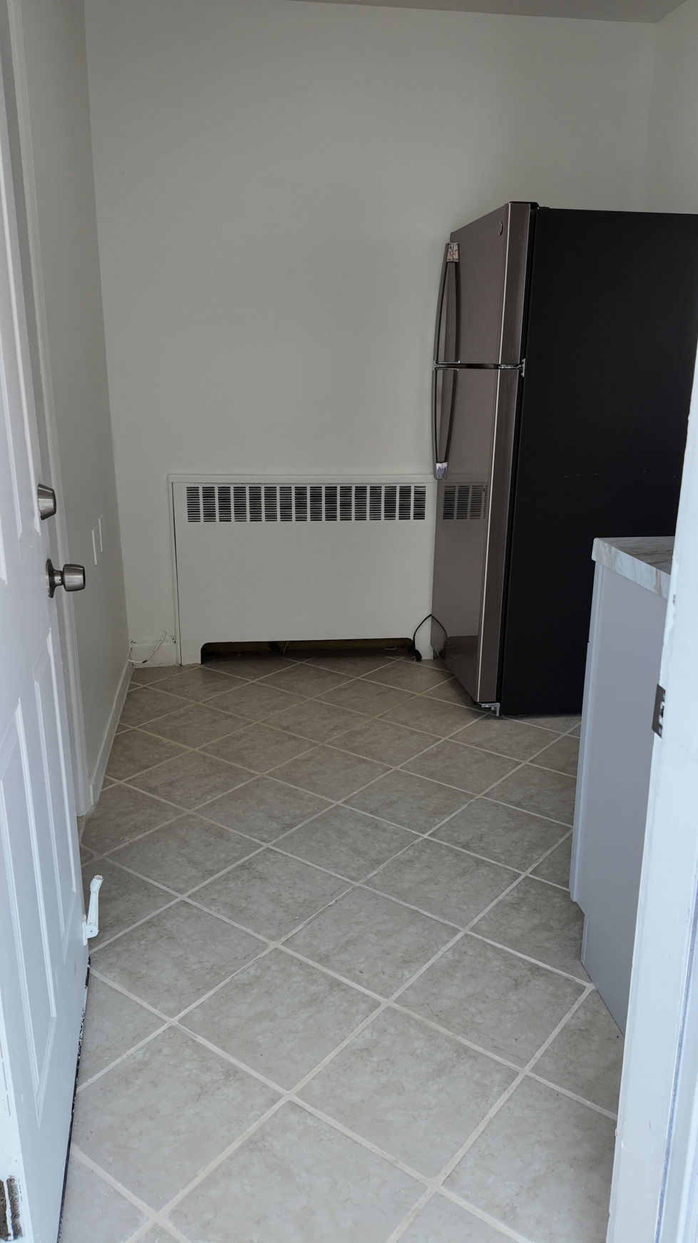 Diagonal tile flooring in a kitchen beside a refrigerator and radiator