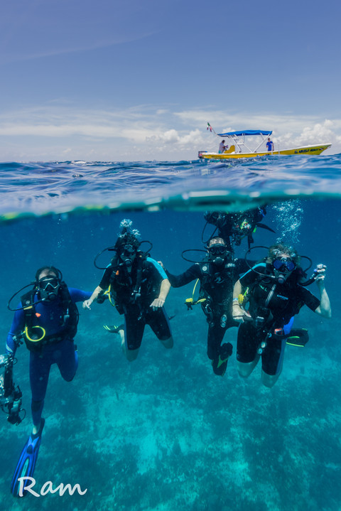 Group of scuba divers underwater with a yellow dive boat floating above near Isla Mujeres.