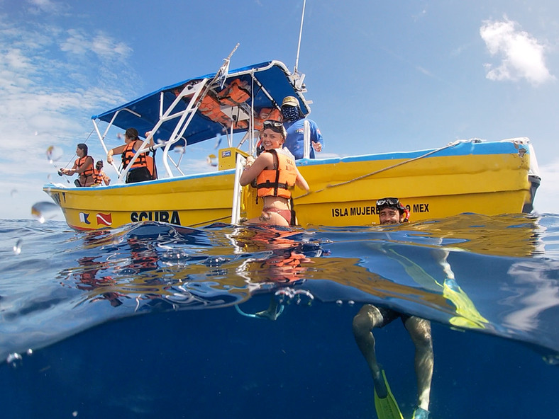 Happy snorkelers boarding a bright yellow boat after a fun tour in Isla Mujeres, Mexico.