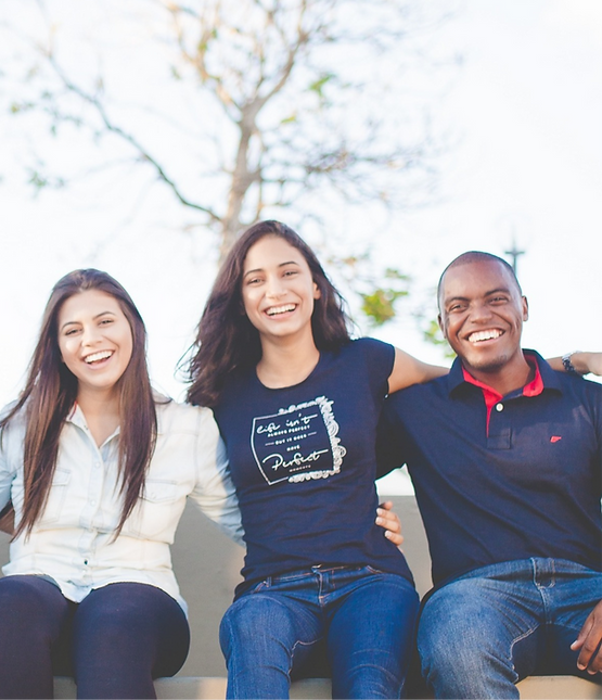 Three people of different ethnicities with their arms around each other, smiling
