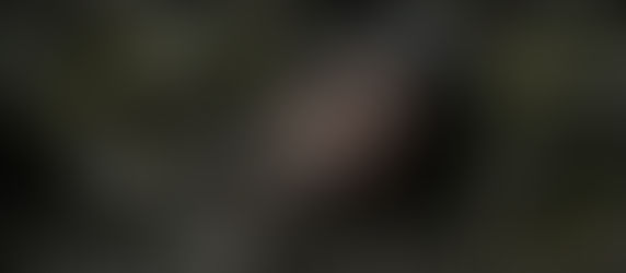 Yüzü çamur ve yaralarla kaplı, sakallı bir adam eski taş kalıntıları arasında yere gömülü şekilde yatıyor. Karanlık ve dramatik atmosferde çekilmiş sinematik bir sahne.