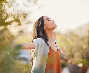 Young latin woman with arms outstretched breathing in fresh air during sunrise at the balc