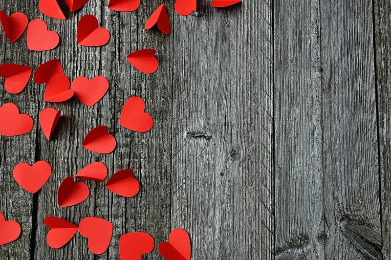 Red paper hearts scattered throughout the left-hand side of a wooden table.