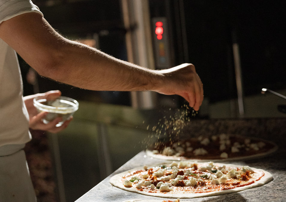 Pizza chef adding cheese to pizzas