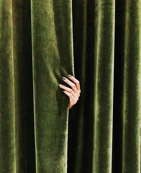 Hand peeking behind a rich, green velvet curtain