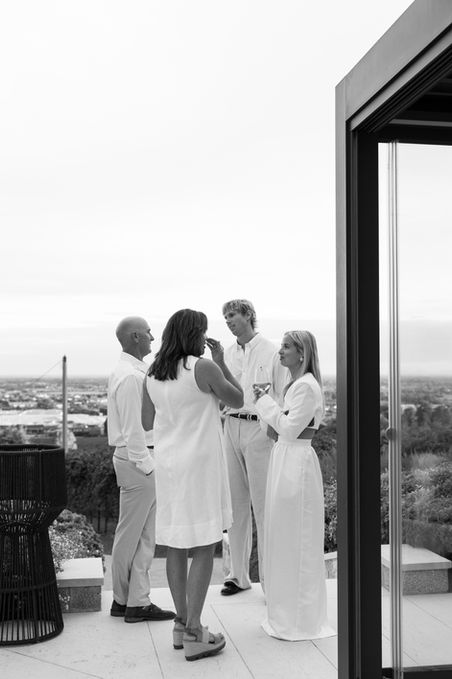 Four people in white outfits converse on patio