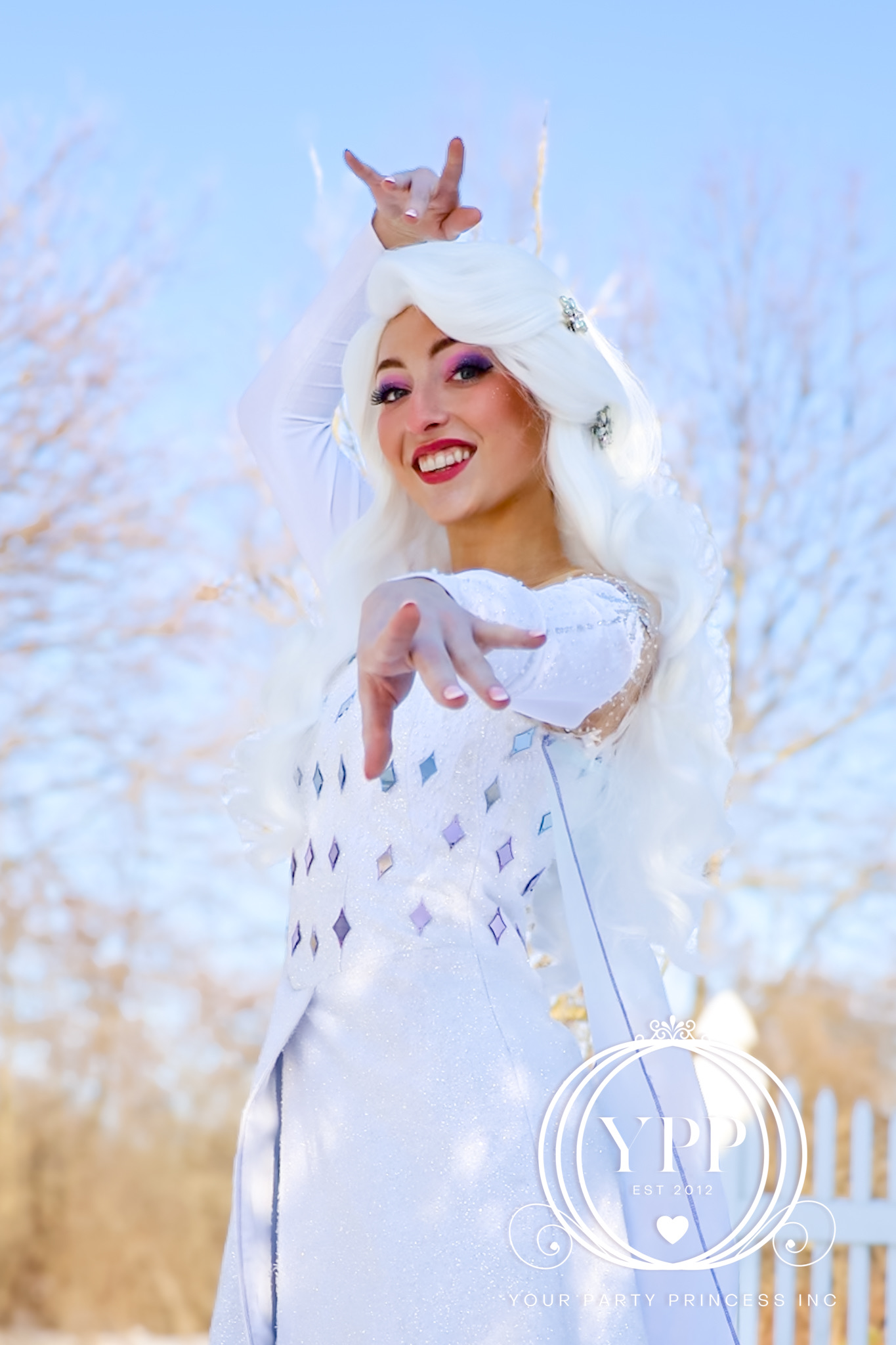 Smiling woman in white costume and wig poses outdoors against blue sky, with YPP EST 2012 Your Party Princess Inc watermark.