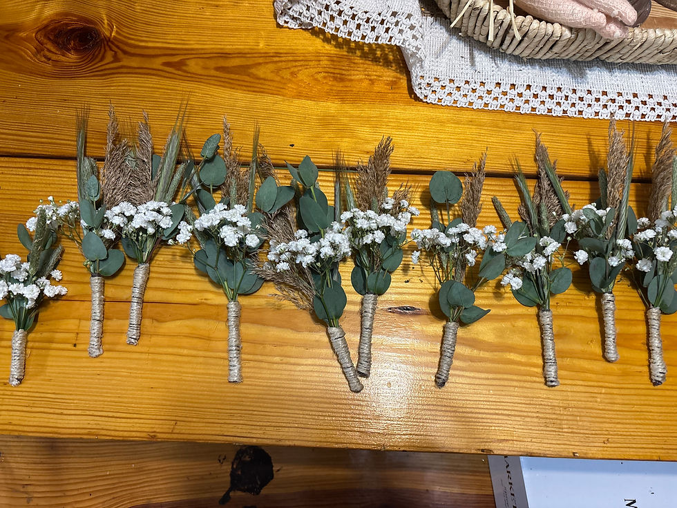 Row of rustic boutonnieres with white baby’s breath, eucalyptus, and dried grasses laid on a honey-colored wooden table