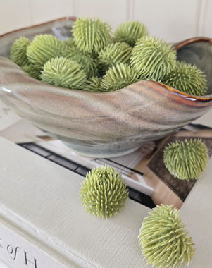 Reactive glazed curled bowl showing beautiful warm colours, on top of an interior book filled with echinops