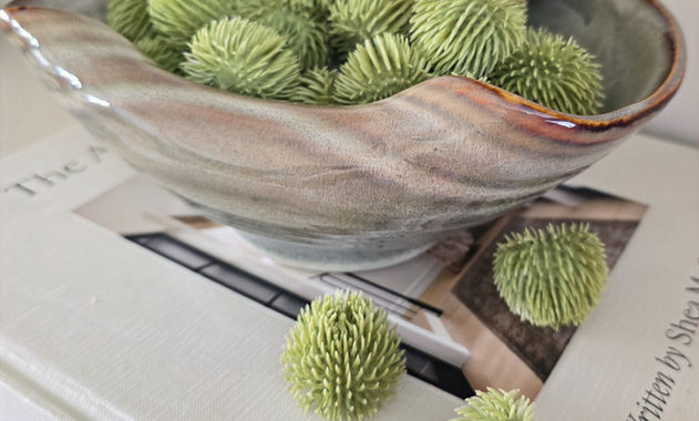 Reactive glazed curled bowl showing beautiful warm colours, on top of an interior book filled with echinops