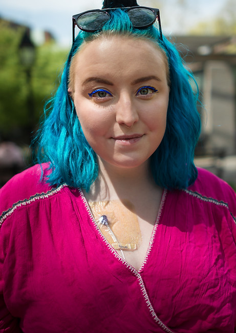 Lucy, a white woman with blue hair, smiles. Her port is visible on her chest.