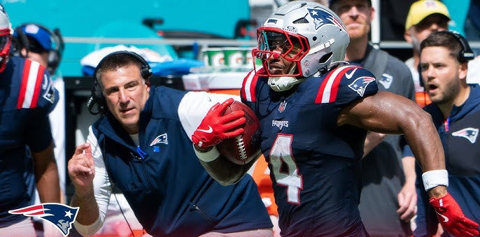 Patriots Head Coach Mike Vrabel running down the sideline while Running Back Antonio Gibson returns a kickoff. Credit to the New England Patriots YouTube page via youtube.com.