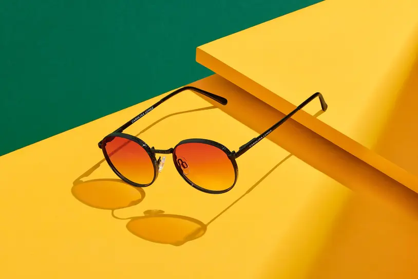 Stylish Carolina Lemke sunglasses with gradient orange lenses displayed against a vibrant yellow and green background. Shot by still life and product photographer in London Celso Marrero."