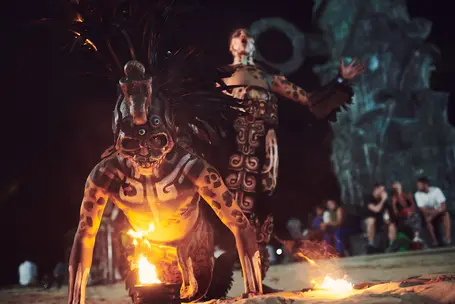 Mayan performer kneeling with fire, surrounded by other performers during a nighttime ritual in Playa del Carmen, Mexico. Photographed by lifestyle photographer Celso Marrero.