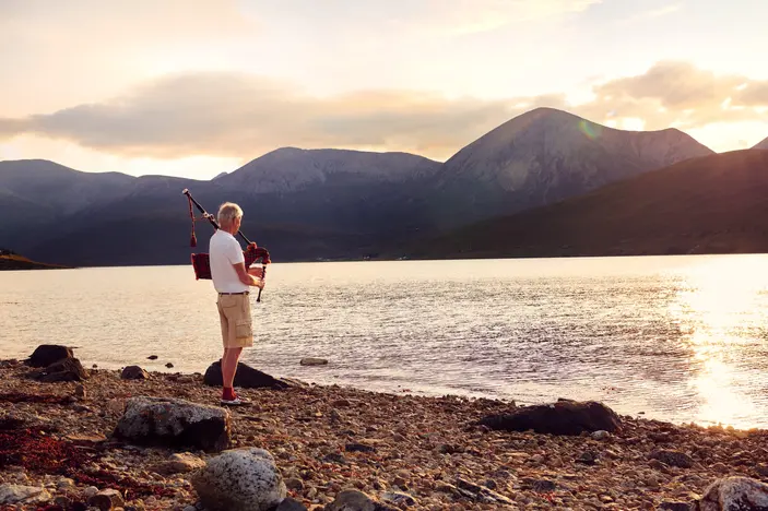 Elderly man playing bagpipes on the shore of the Isle of Skye at sunset, a personal project by lifestyle photographer Celso Marrero.