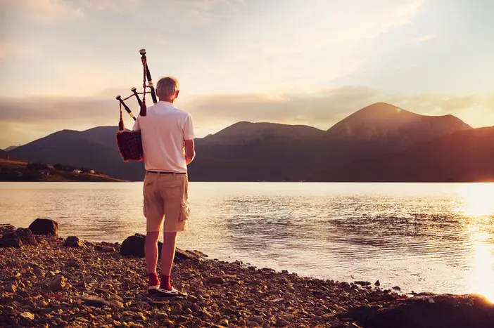 Elderly man playing the bagpipes at the edge of a lake on the Isle of Skye, captured by London-based lifestyle photographer Celso Marrero