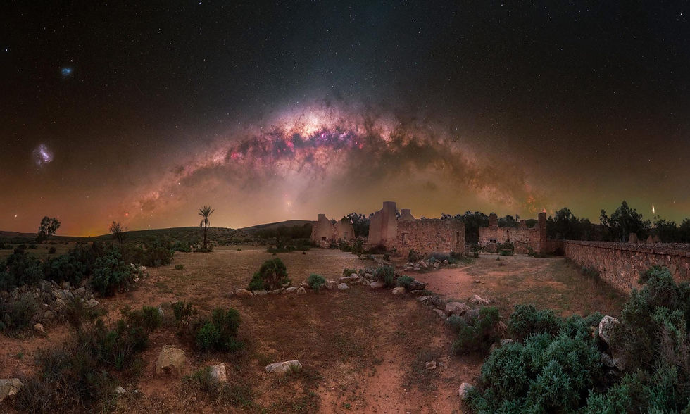Starry sky with the Milky Way over ancient ruins and a barren landscape. Sparse greenery beneath, creating a serene and timeless scene.