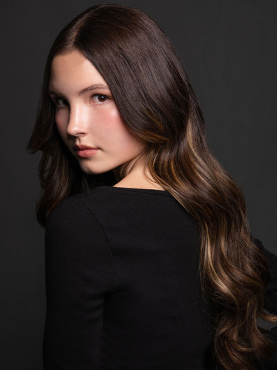 Woman with long brown hair wearing black clothing in a studio portrait