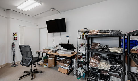 Office space with desk, chair, TV, shelves, and various supplies visible background.