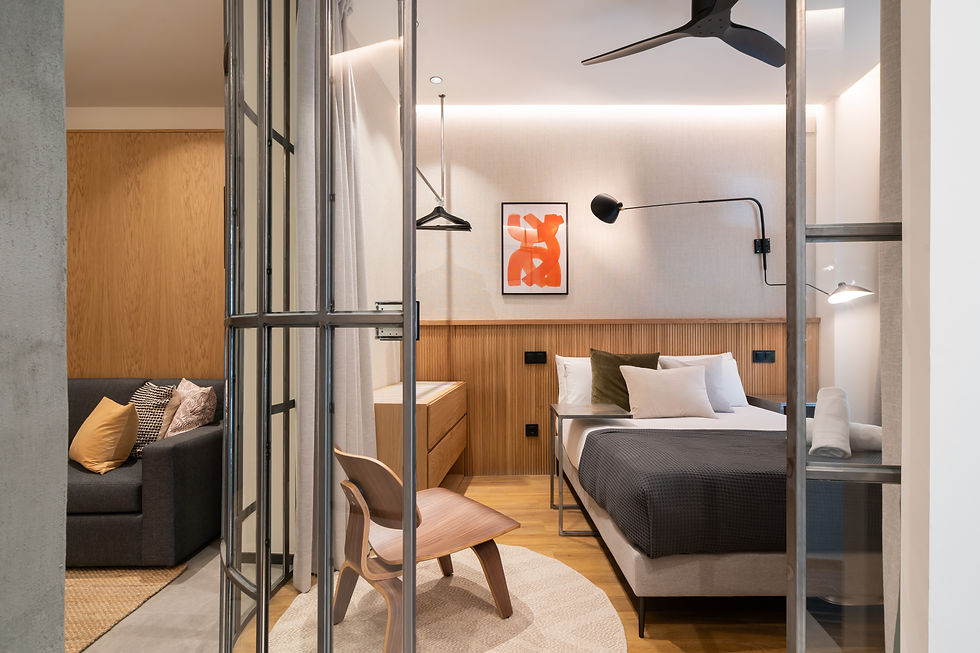 Dormitorio con cama y cristalera de metal y vidrio. Pared con cuadro y detalle de cabeceron con madera. Cama con manta, cojines y toallas.