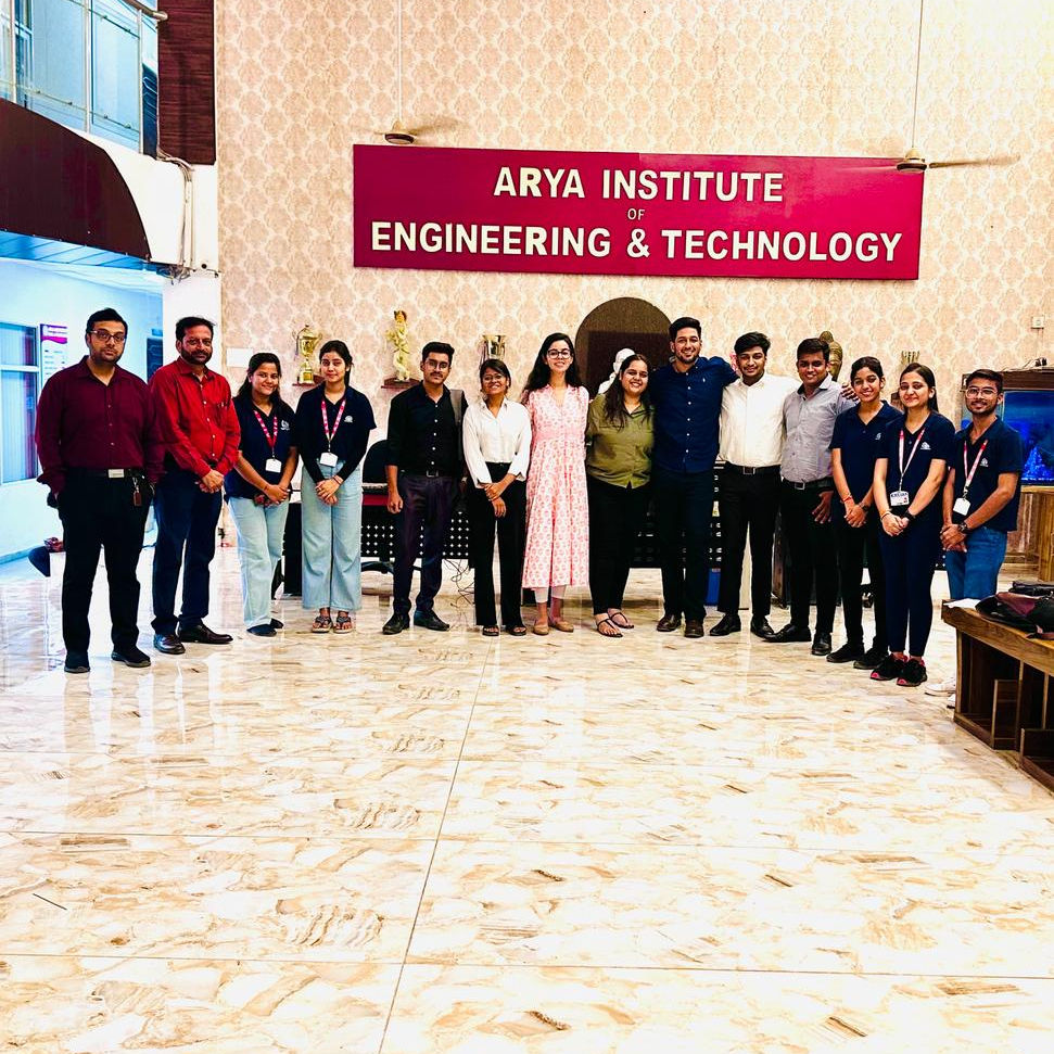 About thirteen people lined up across a bright campus lobby, Mandelbulb team members with students and faculty in lanyards, beneath a large sign reading Arya Institute of Engineering and Technology.