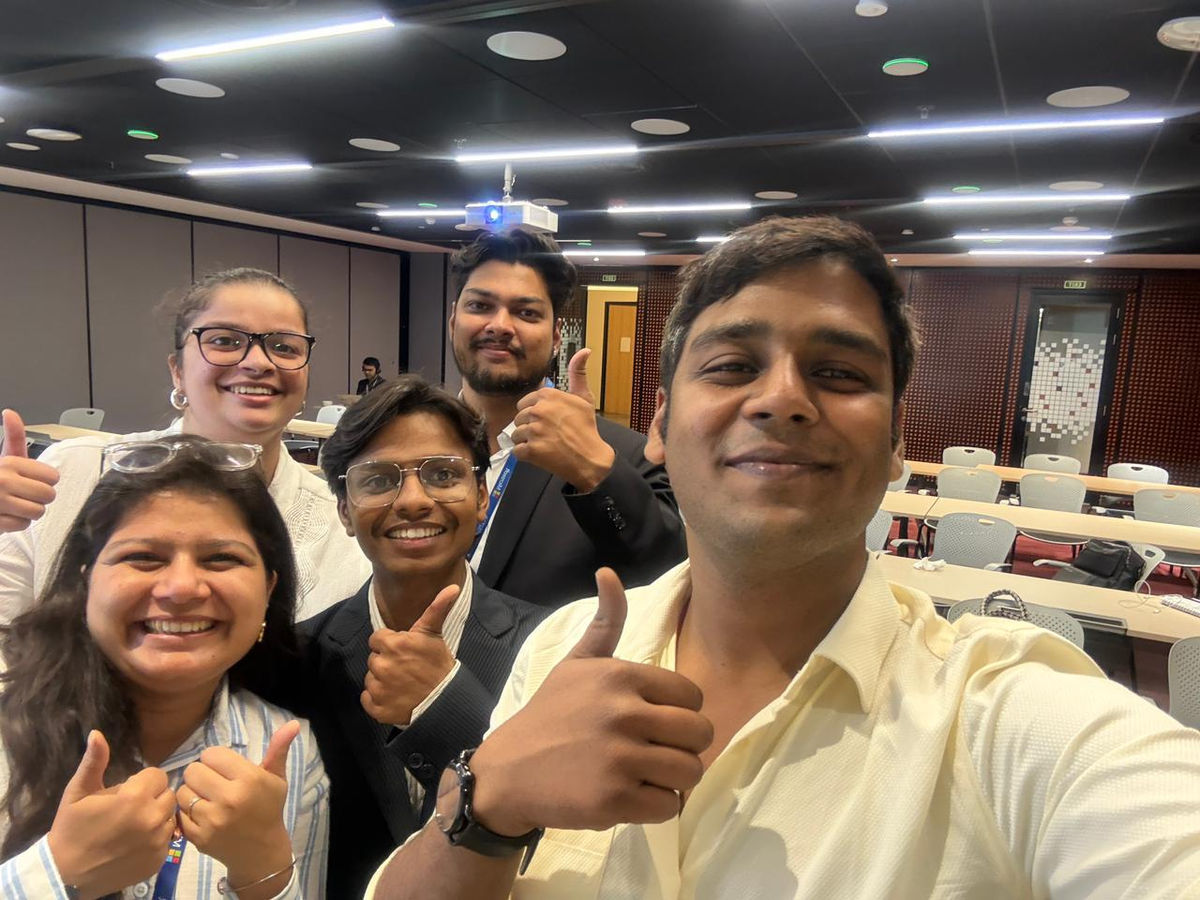 A five person selfie taken in a training auditorium, everyone giving a thumbs up to the camera.