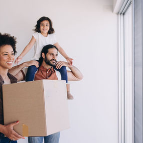 A mixed couple and their daughter mid-moving. The Wife is carryin boxes, while the husband carries their daughter.