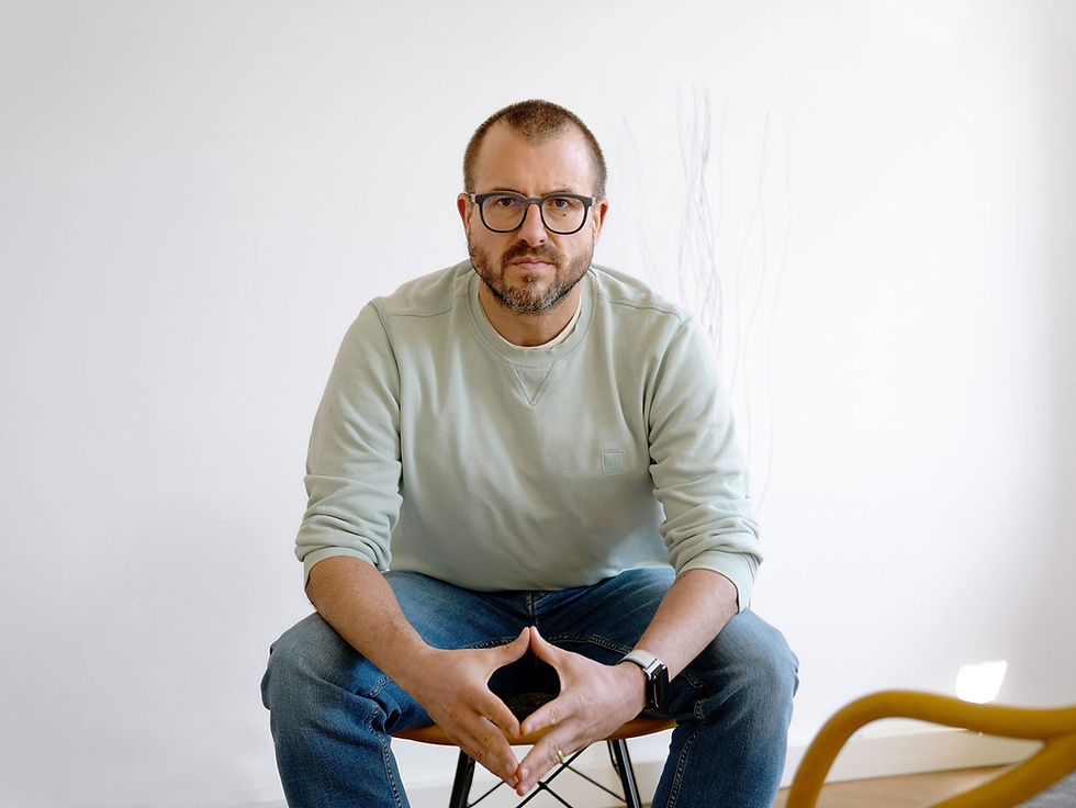 Porträt von Thomas Grupp, Systemischer Business Coach in München, der freundlich lächelnd auf einem Stuhl sitzt.