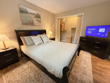 Queen bed, smart TV on the dresser and open closet with linens in a furnished month to month 1 bedroom