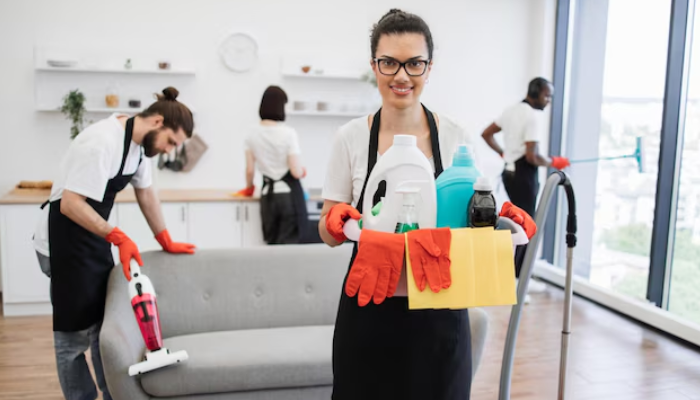 Professional team demonstrating how to start a cleaning business in Las Vegas, holding cleaning supplies while coworkers vacuum and sanitize a modern home interior.
