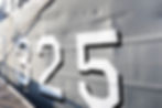 Gray ship hull with large white numbers "325" outlined in black. Sunlight casts shadows, highlighting the ship's textured surface.