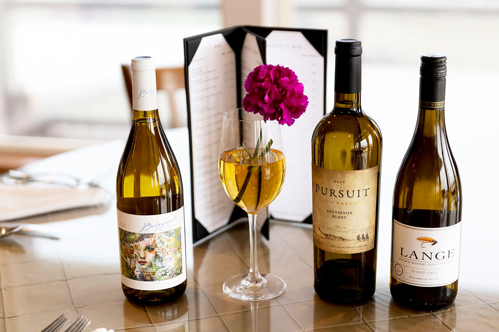A glass of white wine with a violet carnation in it sits on a beautiful table with three bottles of white wine and a leather wine menu