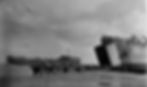 Ships on a beach with open ramps and soldiers unloading. Trucks on sand. Overcast sky with two balloons. "US 325" visible on a ship.
