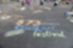 Chalk art festival on pavement with colorful text "573 MAGAZINE 2025", people drawing, rock piles, and casual, creative atmosphere.