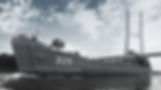 A gray ship marked "325" sails under a large bridge against a partly cloudy sky. An American flag flies at the bow.