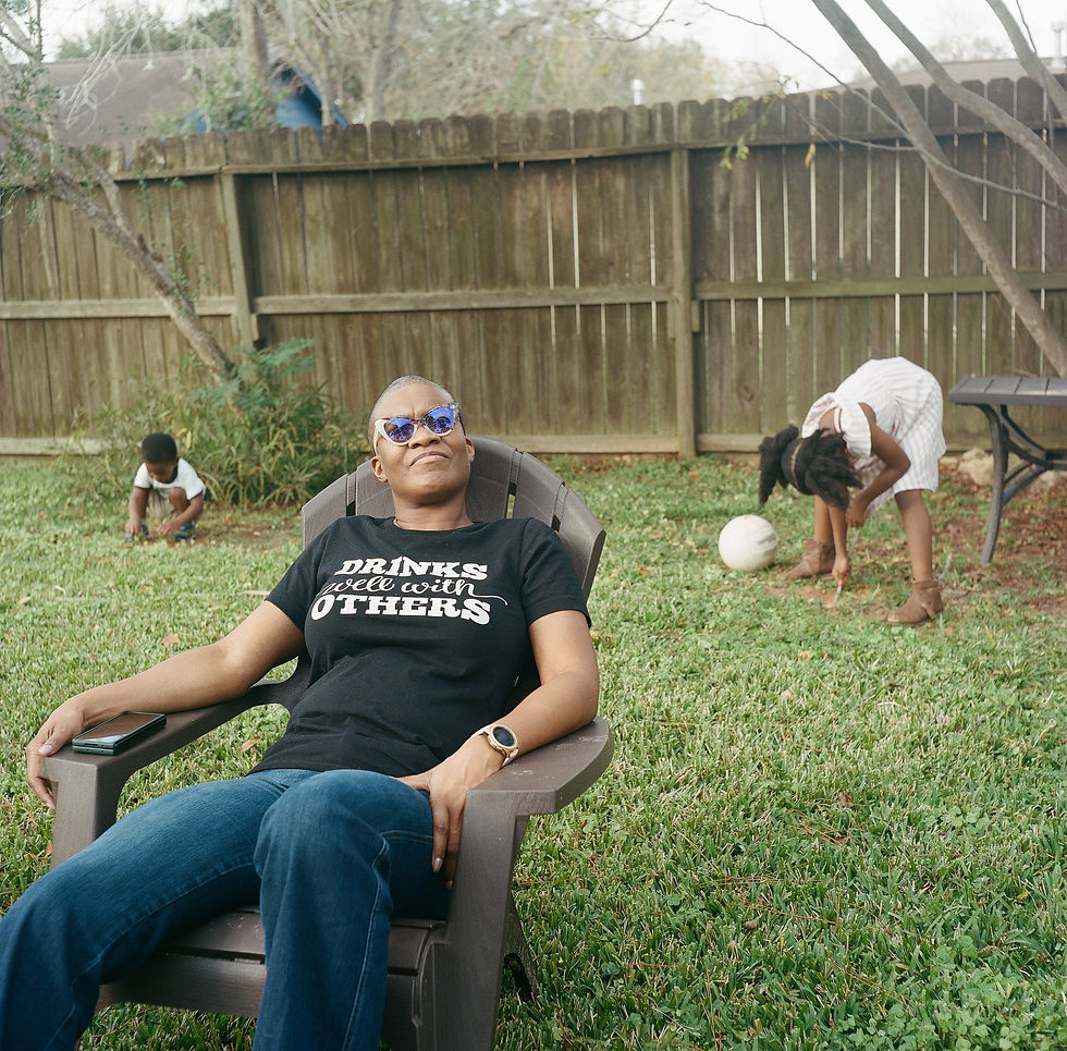 black aunt sitting down in a backyard chair while two black kids play in the background.