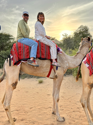 two people sitting in camel with red saddle
