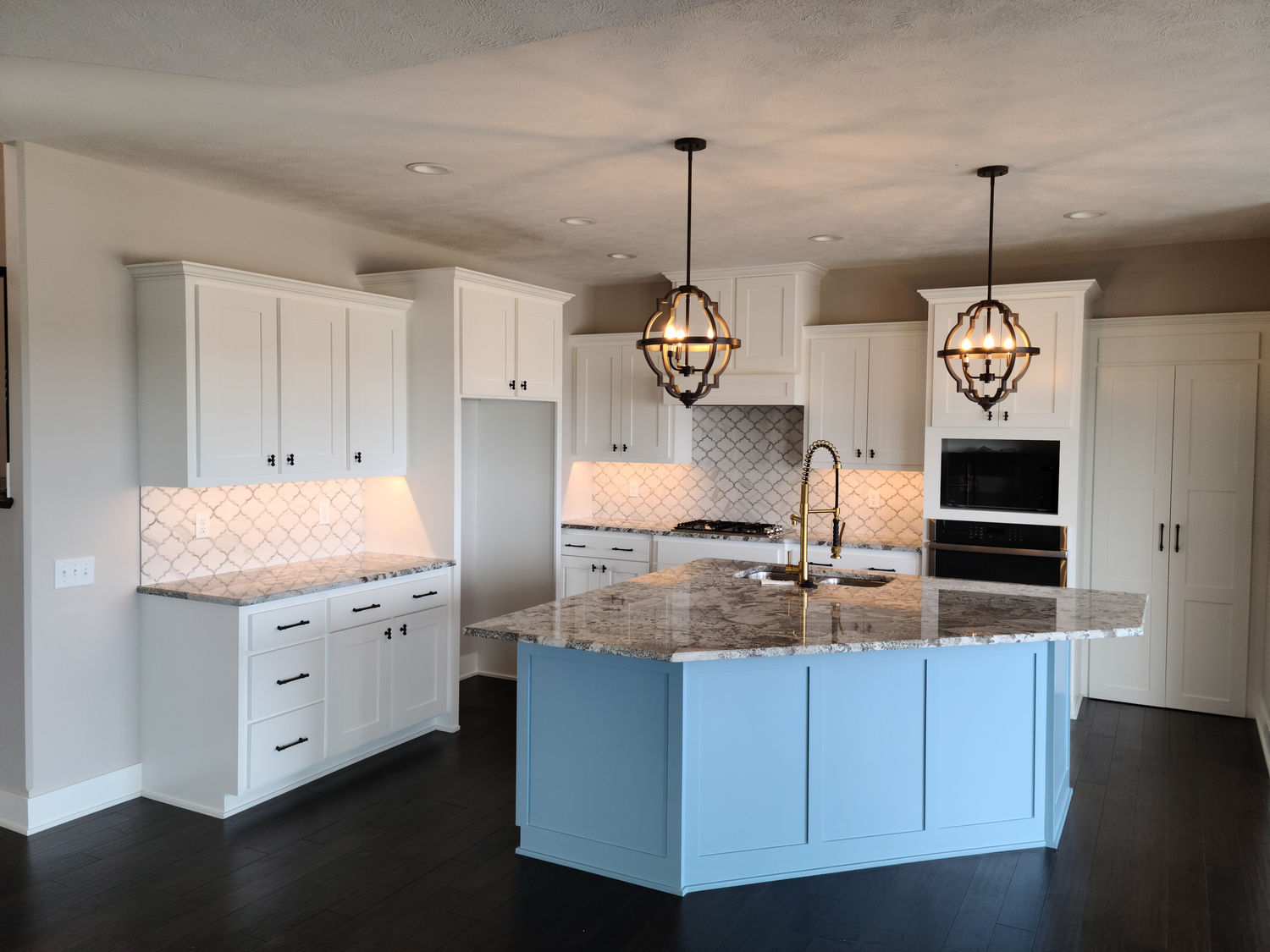 Custom kitchen in an Omaha new construction home with white cabinets, a blue island and glass pendant lights