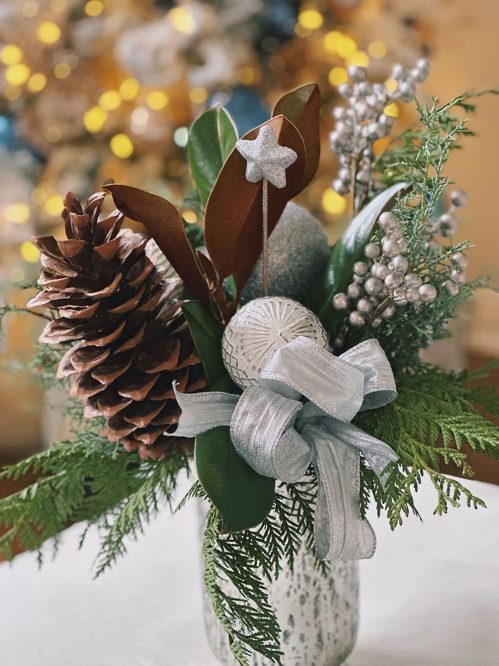 Silver mercury vase filled with winter greens, dried florals, and ornament accents arranged in a festive holiday style