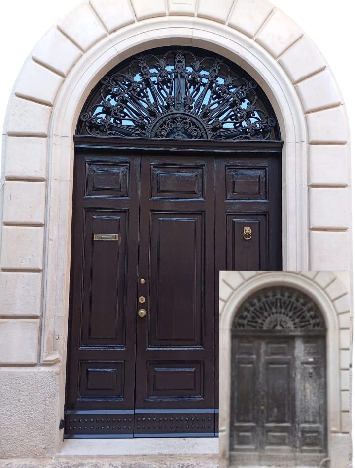 Portone in legno scuro restaurato, con arco superiore decorato in ferro battuto e dettagli scolpiti