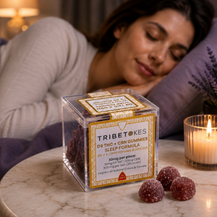 Sleeping woman beside Tribetokes sleep gummies on a marble table, lit candle and lavender in a soft purple bedroom.
