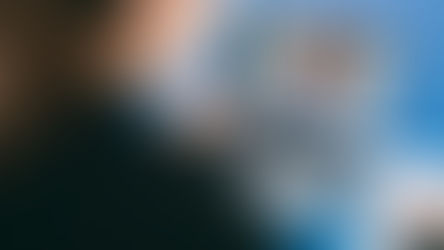 Person video-chatting on a laptop, taking notes on paper. Screen shows two people in a call. Blue table background, focused mood.