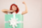 A woman celebrating as she rewards herself with a large gift box, holding it with excitement and happiness. She is dressed stylishly, standing in a bright and cheerful setting.