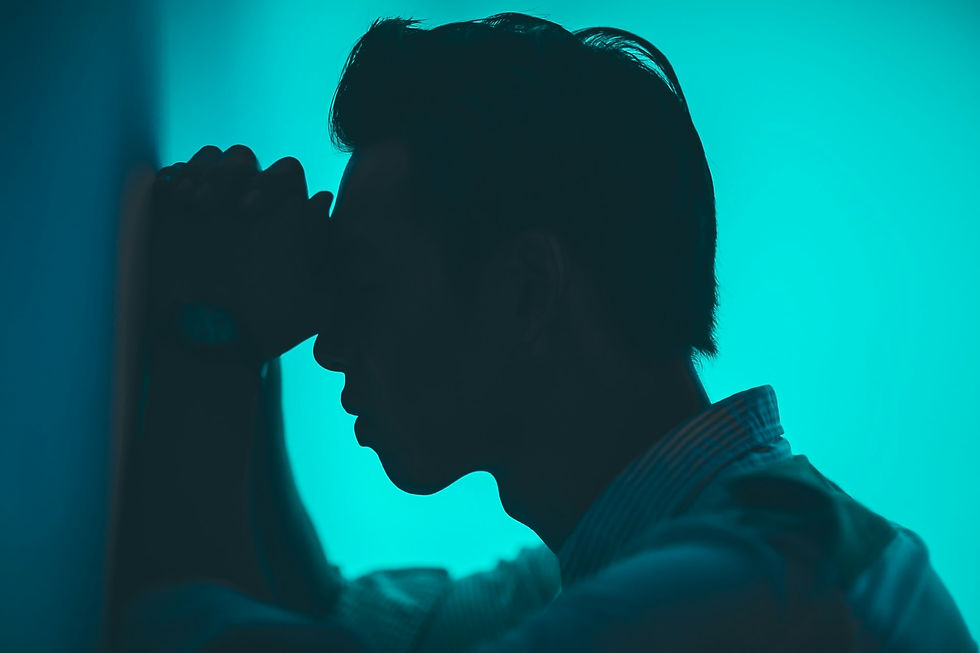 Silhouette of a person leaning against a wall with head bowed and hands clasped, reflecting emotional and physical pain against a teal gradient background.