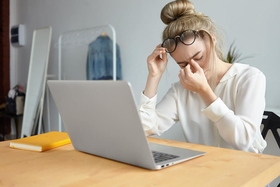 Person at desk with laptop pinching nose bridge, showing discomfort from an eye strain headache while studying.