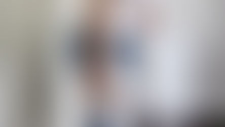 Person in a white shirt and denim shorts holding toilet paper and standing near a white toilet, appearing uncomfortable, illustrating the need for Non Surgical Hemorrhoid Treatment.