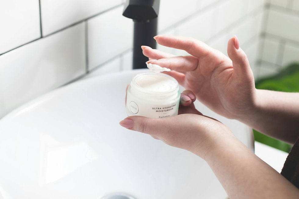Hands applying cream from a jar labeled "Ultra Hydrating Moisturiser" over a white sink. Tile backsplash visible in the background.