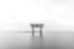 A black-and-white photo of a torii gate standing in still water with distant hills and a cloudy sky, creating a peaceful zen state of mind atmosphere.