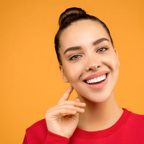 Smiling woman with bun in red sweatshirt poses against a bright orange background, hand resting by her cheek.